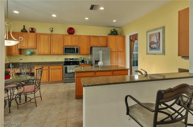 kitchen with stainless steel appliances, kitchen peninsula, dark stone counters, pendant lighting, and a breakfast bar area