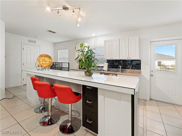 kitchen featuring a center island, tasteful backsplash, light tile patterned flooring, a kitchen bar, and white cabinetry