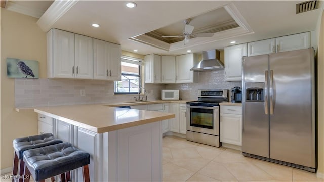 kitchen with wall chimney exhaust hood, a kitchen bar, white cabinetry, and appliances with stainless steel finishes