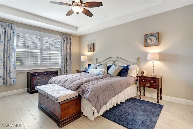 bedroom with a tray ceiling, ceiling fan, and light wood-type flooring