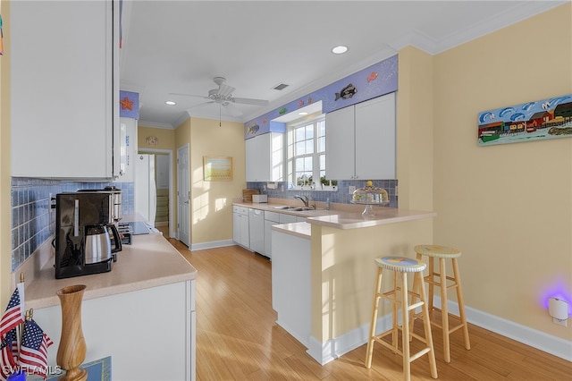 kitchen featuring white cabinets, sink, light hardwood / wood-style flooring, tasteful backsplash, and a kitchen bar