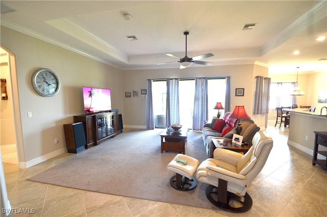 tiled living room featuring ceiling fan, ornamental molding, and a tray ceiling