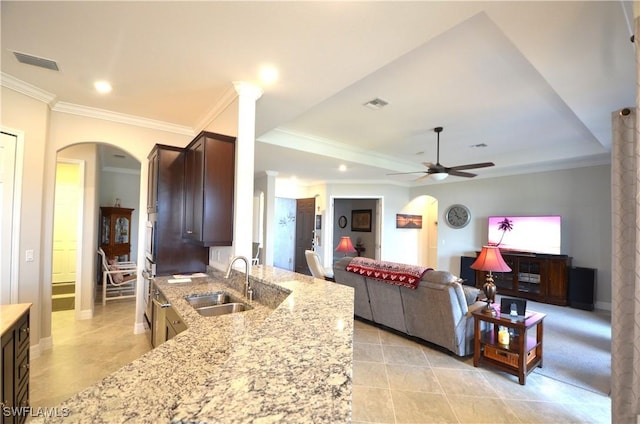 kitchen with light stone counters, ornamental molding, dark brown cabinetry, ceiling fan, and sink