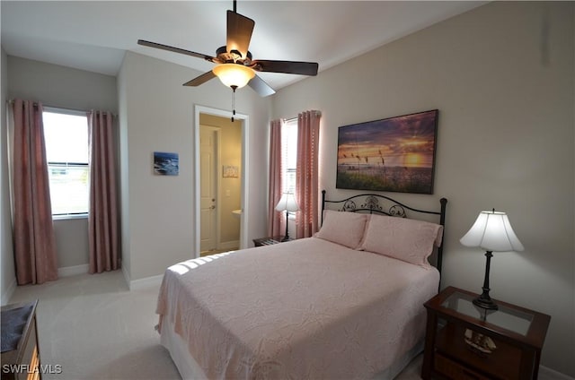 bedroom with light carpet, connected bathroom, multiple windows, and ceiling fan