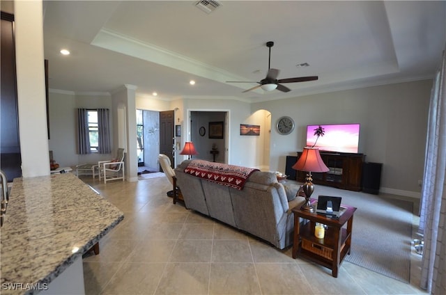 tiled living room with a raised ceiling, ceiling fan, and ornamental molding