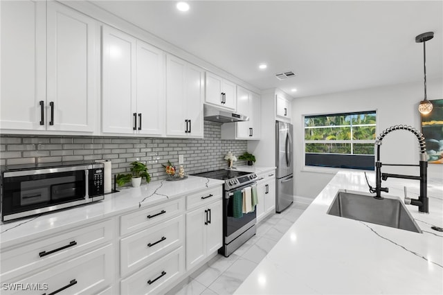 kitchen featuring pendant lighting, appliances with stainless steel finishes, white cabinets, sink, and light stone counters