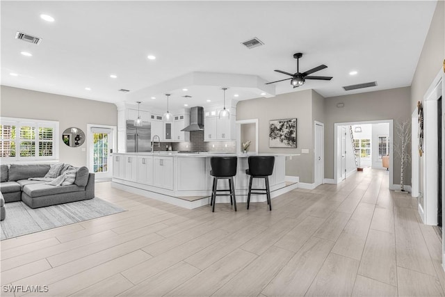 kitchen featuring open floor plan, stainless steel built in refrigerator, light countertops, wall chimney range hood, and pendant lighting