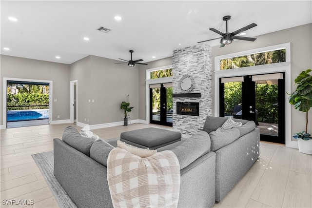 living area featuring a fireplace, visible vents, a ceiling fan, and french doors