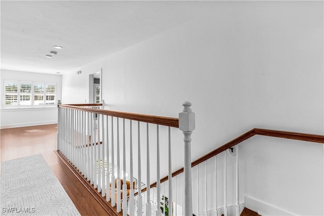 hallway with wood finished floors, an upstairs landing, and baseboards