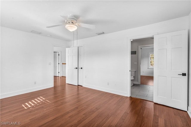 unfurnished bedroom featuring visible vents, ensuite bathroom, baseboards, and wood finished floors