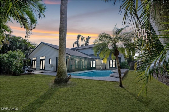 back of house at dusk with a yard, a patio area, and an outdoor pool