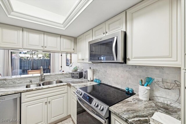 kitchen with a raised ceiling, sink, stainless steel appliances, and an inviting chandelier