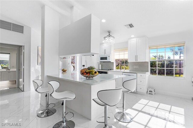 kitchen with white cabinetry, a wealth of natural light, a breakfast bar, and white appliances