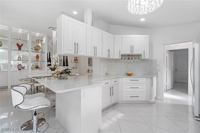 kitchen with kitchen peninsula, a kitchen bar, white cabinetry, stainless steel refrigerator, and a chandelier