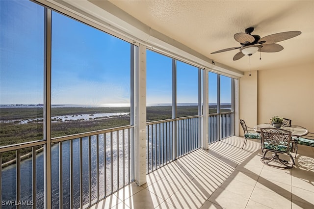 unfurnished sunroom featuring ceiling fan and a water view