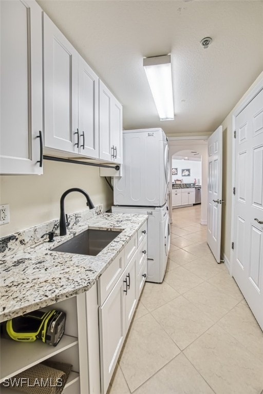 kitchen with light stone countertops, sink, light tile patterned floors, stacked washer / drying machine, and white cabinets