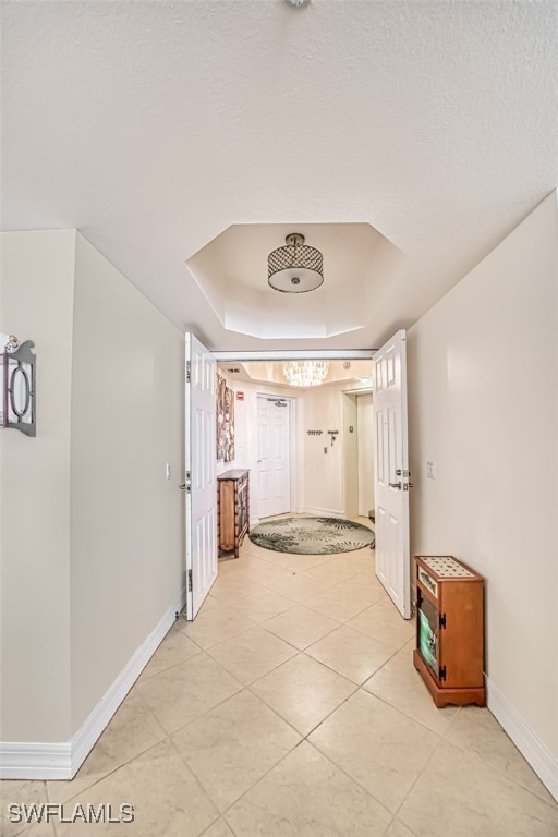 corridor with light tile patterned floors, a textured ceiling, and a raised ceiling