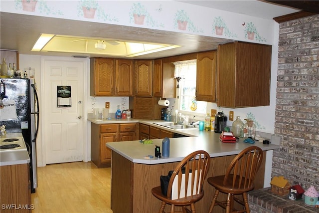 kitchen featuring sink, brick wall, kitchen peninsula, refrigerator, and light hardwood / wood-style floors