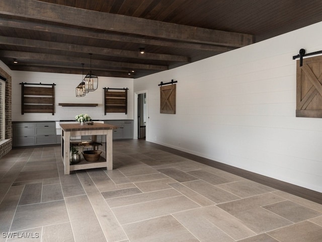 kitchen featuring beam ceiling, a barn door, gray cabinetry, and hanging light fixtures