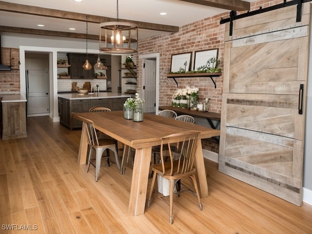 dining room with a barn door, light hardwood / wood-style flooring, a notable chandelier, and brick wall