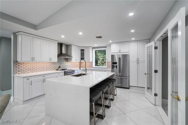 kitchen with sink, appliances with stainless steel finishes, wall chimney range hood, a kitchen island with sink, and white cabinets