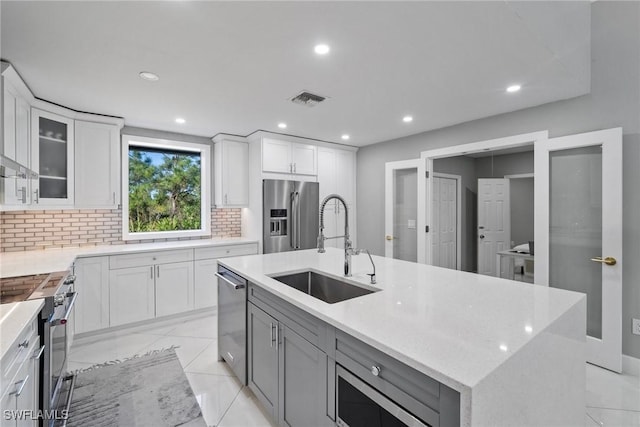 kitchen featuring appliances with stainless steel finishes, tasteful backsplash, sink, white cabinets, and a center island with sink