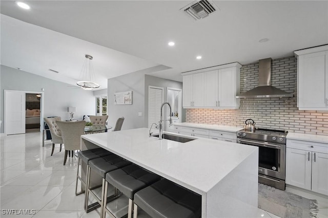 kitchen with stainless steel range with electric stovetop, sink, wall chimney exhaust hood, and a center island with sink