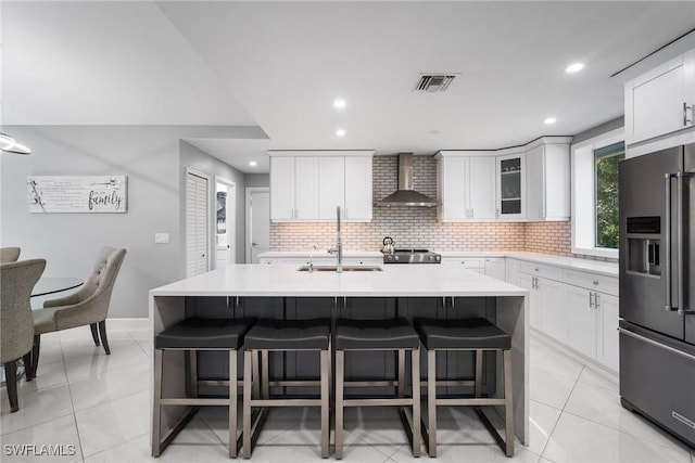 kitchen featuring wall chimney range hood, high end refrigerator, a sink, and a kitchen breakfast bar