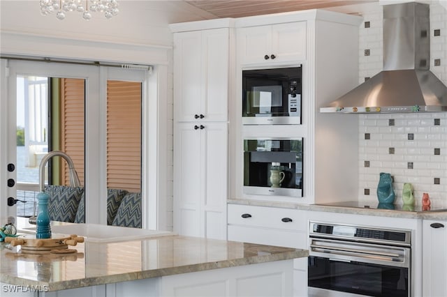 kitchen with decorative backsplash, stainless steel oven, white cabinets, and wall chimney range hood