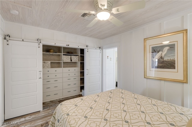 bedroom featuring ceiling fan, wooden ceiling, a barn door, light hardwood / wood-style floors, and a closet