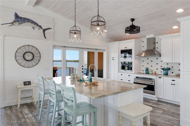 kitchen featuring white cabinetry, wall chimney range hood, oven, vaulted ceiling, and a water view