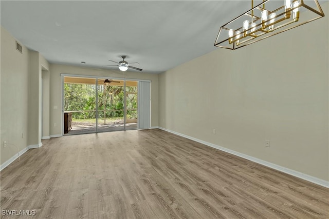 spare room with ceiling fan with notable chandelier and light wood-type flooring