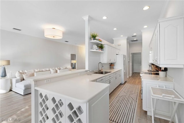 kitchen featuring sink, kitchen peninsula, a kitchen bar, white cabinets, and light wood-type flooring