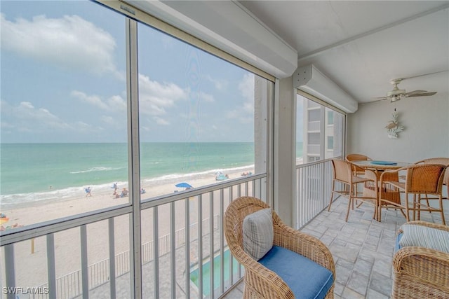 sunroom with ceiling fan, a water view, and a beach view