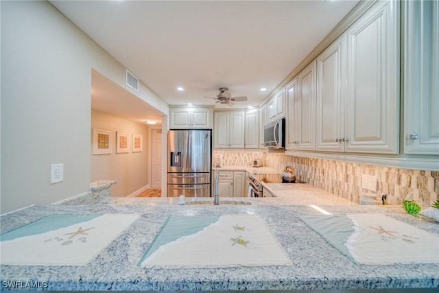 kitchen featuring backsplash, ceiling fan, appliances with stainless steel finishes, light stone counters, and kitchen peninsula