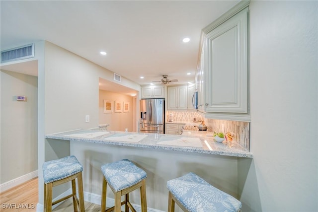 kitchen featuring light stone countertops, stainless steel appliances, kitchen peninsula, a breakfast bar area, and decorative backsplash