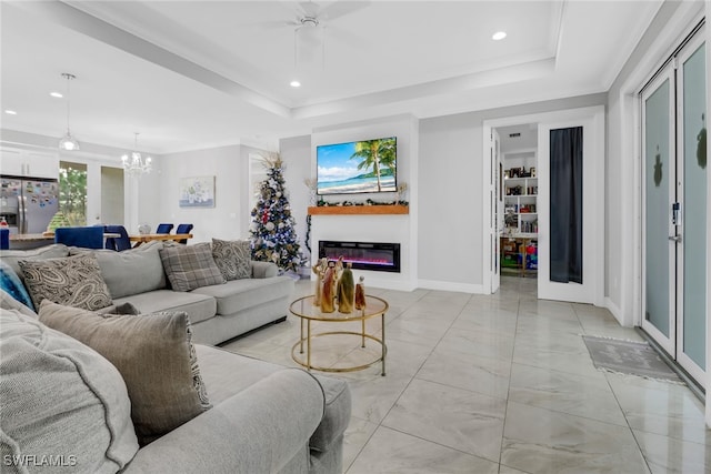 living room featuring ceiling fan with notable chandelier, a raised ceiling, and crown molding