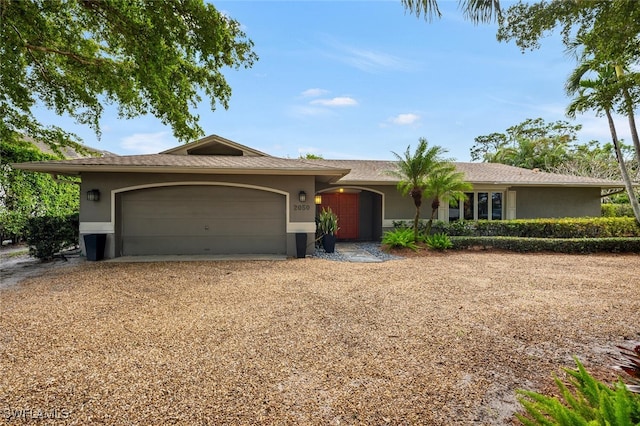 ranch-style house with a garage, dirt driveway, and stucco siding