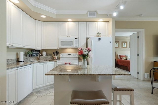 kitchen featuring light stone countertops, a center island, white cabinets, and white appliances