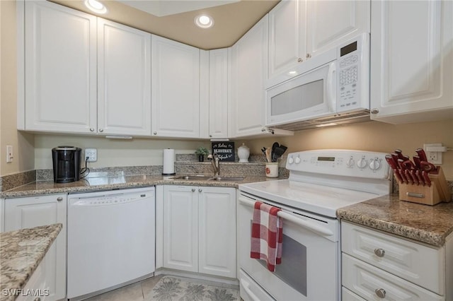 kitchen featuring white appliances, white cabinets, sink, light tile patterned floors, and light stone counters