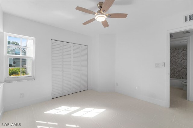 unfurnished bedroom featuring ceiling fan, ensuite bath, a closet, and light tile patterned flooring