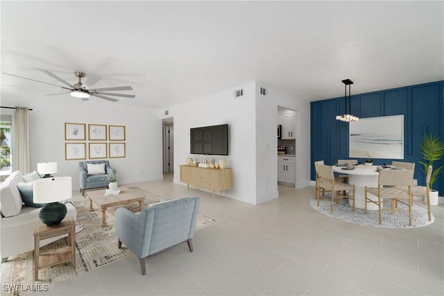 tiled living room with ceiling fan with notable chandelier