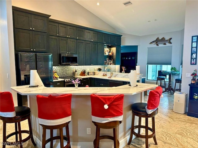 kitchen with stainless steel appliances, vaulted ceiling, a breakfast bar area, and an island with sink