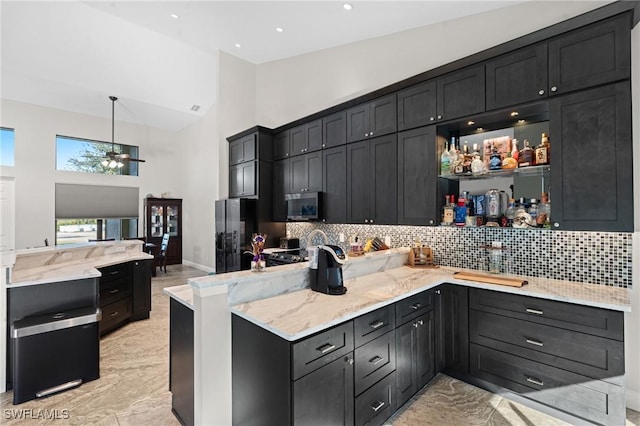 kitchen with high vaulted ceiling, stainless steel microwave, hanging light fixtures, dark cabinets, and a peninsula