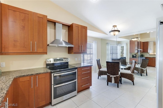 kitchen featuring vaulted ceiling, decorative light fixtures, dark stone counters, double oven range, and wall chimney range hood