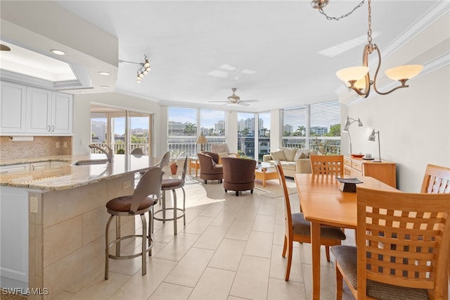 dining area with light tile patterned flooring, ceiling fan with notable chandelier, crown molding, and sink