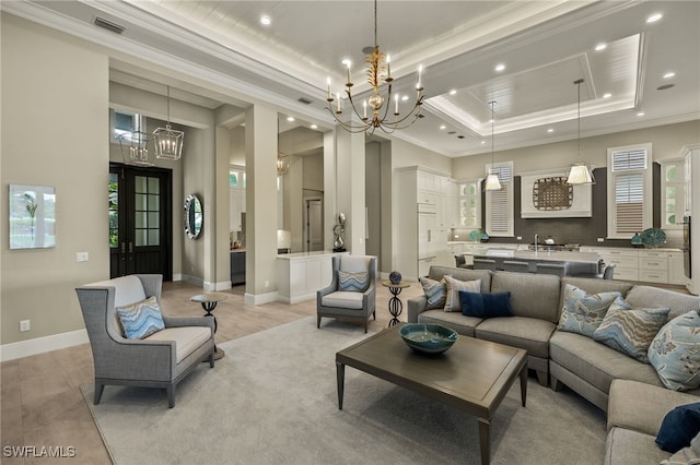 living room featuring a raised ceiling, crown molding, light hardwood / wood-style flooring, and an inviting chandelier