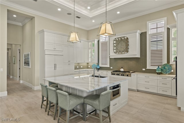 kitchen featuring appliances with stainless steel finishes, a kitchen island with sink, sink, decorative light fixtures, and white cabinetry