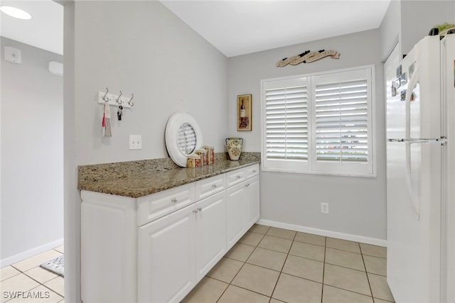 kitchen with white cabinets, dark stone counters, light tile patterned floors, and white refrigerator