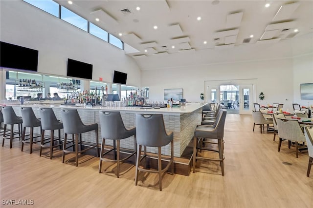 bar with a towering ceiling and light hardwood / wood-style flooring